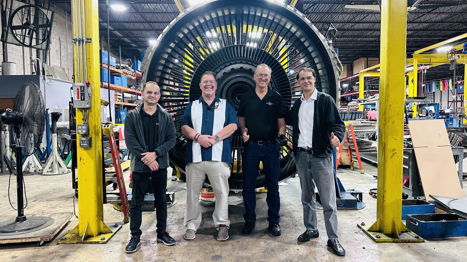 A team standing in front of a jet engine in a maintenance shop